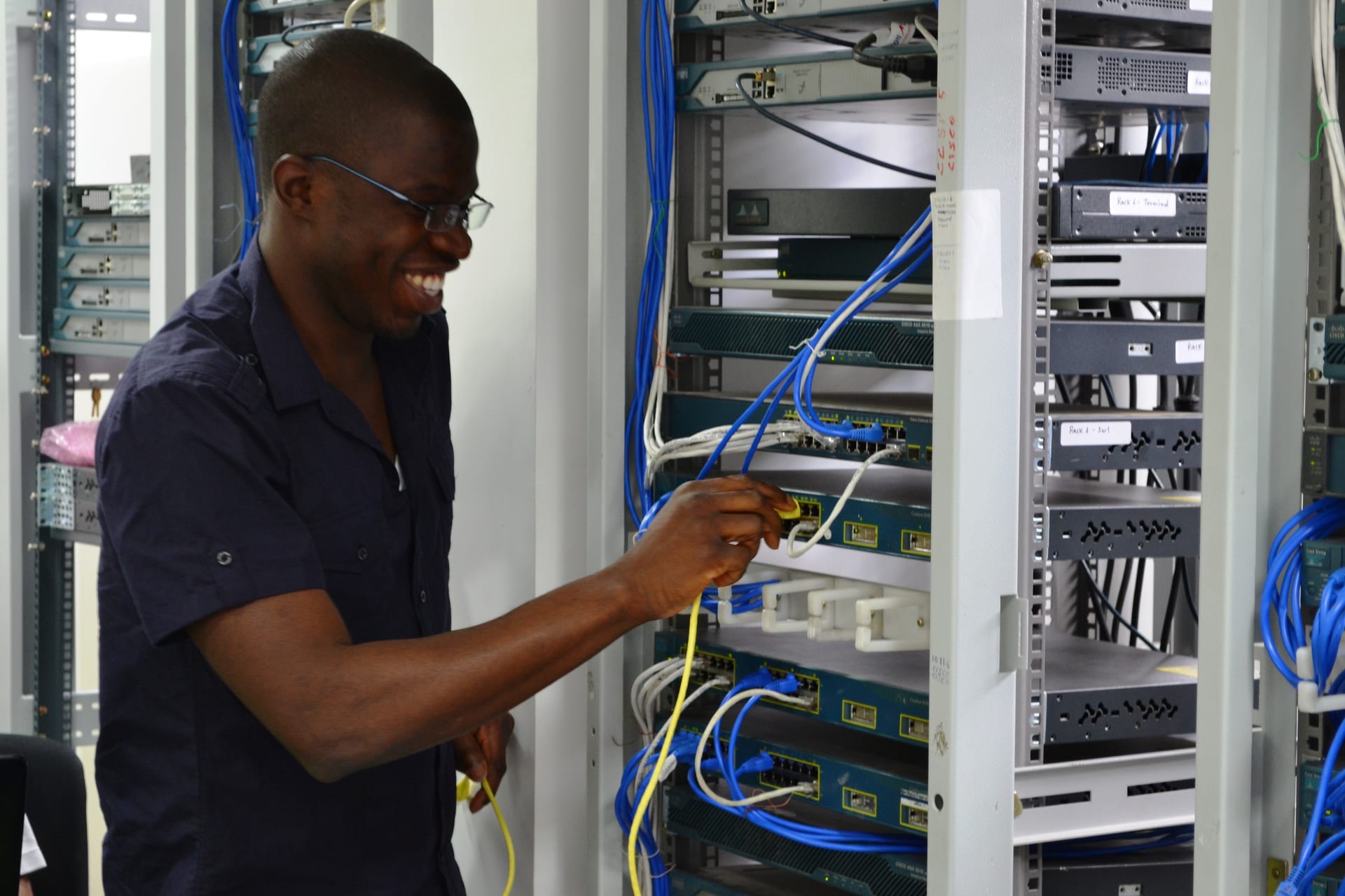 Student doing hands-on Cisco rack cabling — yellow and blue console cables visible